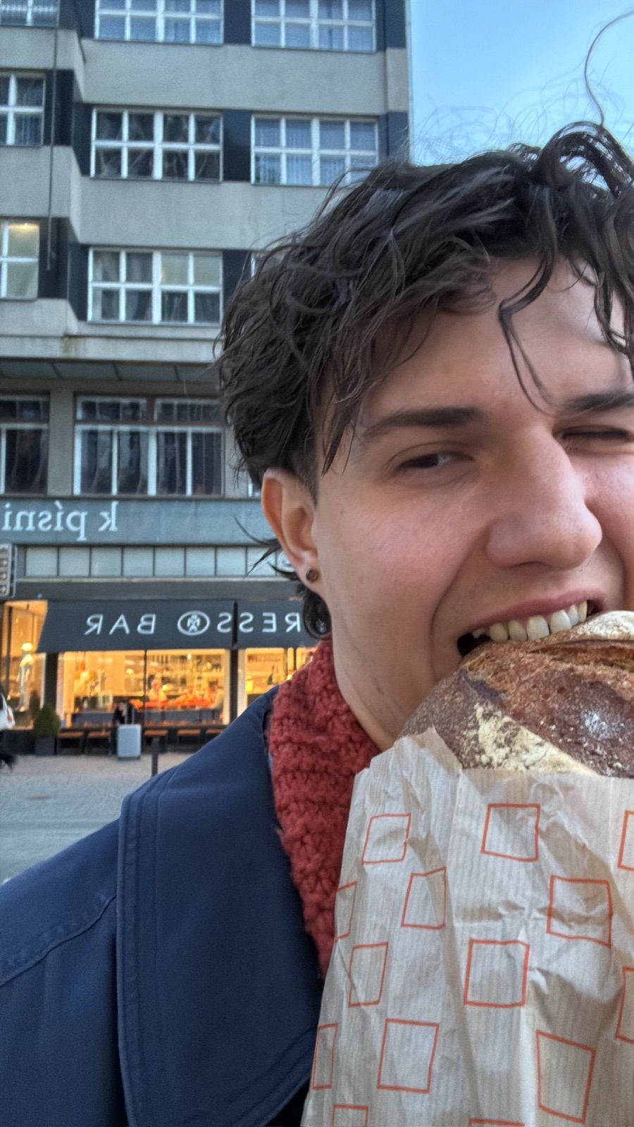 Grinning while biting into a big loaf of sourdough on the street at dusk