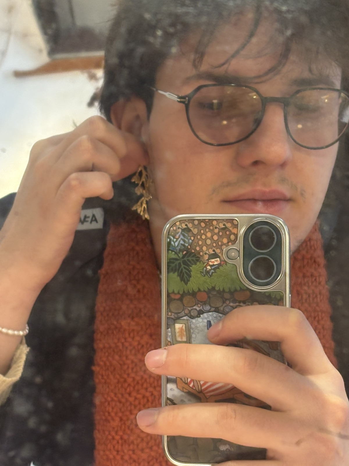 Mirror selfie in a shop, holding a gold leaf-shaped earring up to one ear